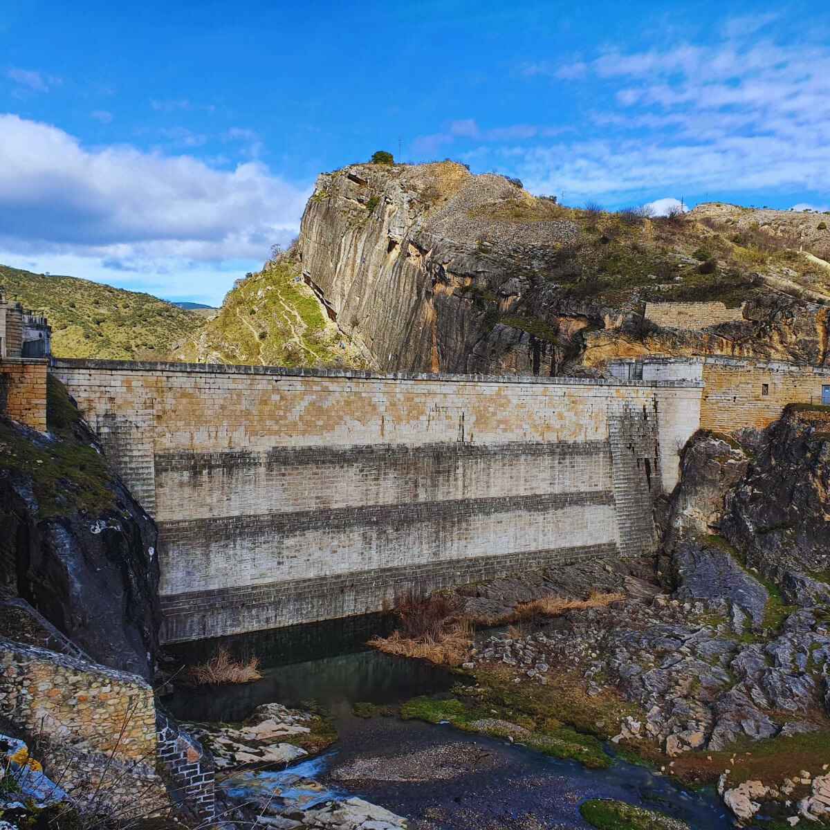 Estamos ante la etapa final de nuestro sendero de gran recorrido GR 10, con el que hemos recorrido la Comunidad de Madrid de Oeste a Este, pasando por las zonas montañosas mas reconocibles del territorio, y algunas otras menos relevantes pero no de menor importancia y belleza. Comenzamos en el Pueblo de Patones de Arriba, localidad pintoresca que alberga una arquitectura tradicional y donde podemos desayunar en sus restaurantes para coger fuerzas ante la caminata. Esta localidad se dice que no fueron capaces de encontrarla las tropas de Napoleon por lo escondida que está!!! Nos ponemos en marcha y abandonamos la población, los caminos están perfectamente visibles pues la mayor parte del recorrido son accesos del Canal de Isabel II, que los utilizan para mantener las instalaciones que veremos en todo momento, de canalización del agua que luego consumimos en nuestros hogares, pues no olvidemos que tenemos muy cerca el embalse de El Atazar, que es uno de los grandes depositos de nuestro agua de consumo. Seguimos avanzado, viendo las almenaras y tuberías que conforman dichas construcciones hidráulicas…y casi sin darnos cuenta y con poco esfuerzo, pues el tramo en cuestión es muy corto y con poco desnivel, estaremos en las inmediaciones del Pontón de la Oliva. Esta presa que está sin uso, pues se construyó sobre una base de roca caliza que reina en esta zona y el agua se filtra, por lo que no es posible embalsar agua, pero que si vamos en épocas de lluvias o deshielo, veremos como atraviesa el agua con fuerza por sus desagües y es digno de ver el espectáculo que nos ofrece el liquido elemento con su fuerza y su ruido ensordecedor. Aquí termina nuestro periplo por el GR 10, pues es el limite provincial, si deseamos seguir ya entramos en Castilla La Mancha donde podremos avanzar en nuestro recorrido.